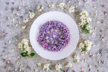 Obraz na płótnie Canvas Served plate with purple and white lilac flowers on gray concrete background, top view. Spring season concept with minimal design.