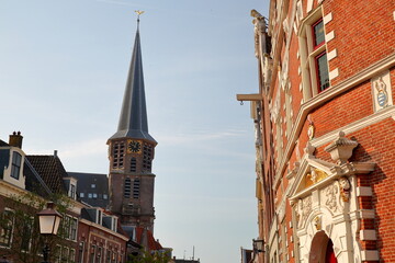 Obraz premium The colorful facades of historic houses located along Kerkstraat street in Hoorn, Netherlands, with the bell tower of Grote Kerk church on the left and the facade of Ceciliakapel (built in 1472)