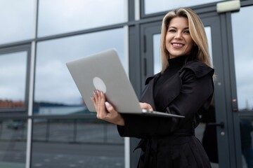 successfully confident businesswoman works online on a laptop against the backdrop of an office building