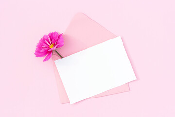 White blank card, pink envelope and flowers on pink background. Minimal style. Top view Flat lay Mockup