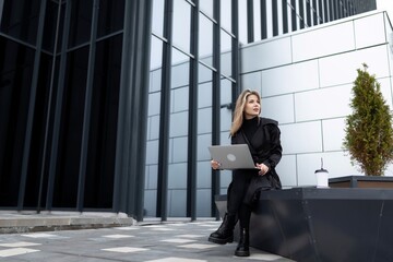 woman businessman working online next to an office building outdoors with a laptop in her hands