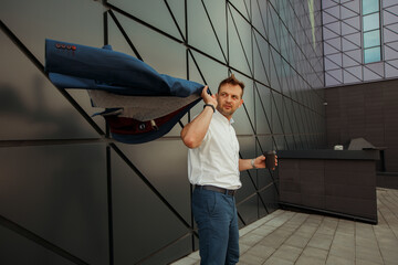 A young businessman man in a jacket near the facade of a business center