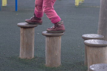 A child walks on a wooden log in a children's park, a kid overcomes obstacles, plays on a children's playground