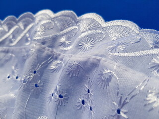 Wavy white lace batiste with a floral print, in the sun, on a blue background - obrazy, fototapety, plakaty
