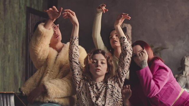 Slowmo of four young fancy multiethnic friends in eccentric vintage outfits dancing vogue for camera in dark authentic studio