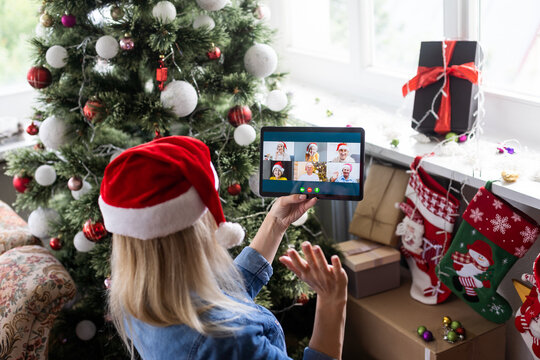 Christmas online holiday. Happy woman having video call with their family or friends. Young woman uses a digital tablet near decorated festive tree at home. Virtual meeting