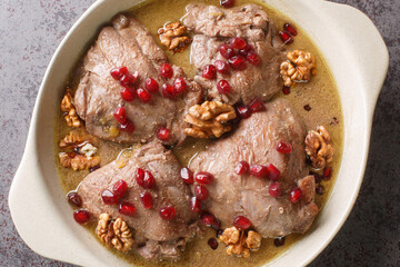 Fesenjan is a simple slowly cooked Iranian stew featuring ground walnuts, pomegranate molasses and chicken thighs close-up in a pan on the table. Horizontal top view from above