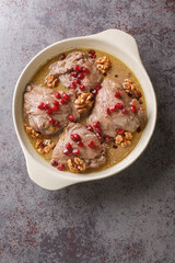 Fesenjan is an Iranian pomegranate and chicken stew made with ground walnuts, onions, squash, cinnamon, and pomegranate molasses close-up in a pan on the table. Vertical top view from above