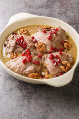 Fesenjan is an Iranian pomegranate and chicken stew made with ground walnuts, onions, squash, cinnamon, and pomegranate molasses close-up in a pan on the table. Vertical