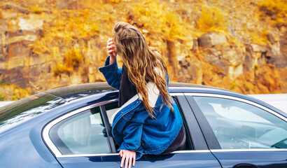 Young happy girl leans out of the car window during a trip. Gold autumn. The concept of freedom.