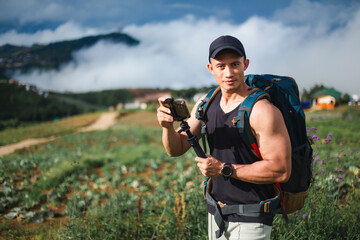 Asian tourist man taking photo on the top of mountains during vacation trip with beautiful sky and fog on background. Traveler blogger with backpack using smart phone and looking at camera. 