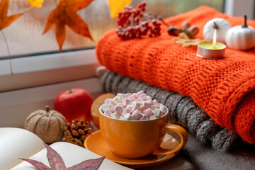a yellow  marshmallow cup with a saucer on autumn leaves with an orange scarf a candle a cone acornes notebook pumpkin apples  on the windowsill in rainy weather