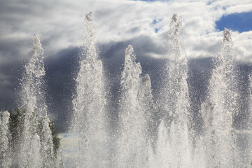 Water streams from a fountain against a cloudy sky.