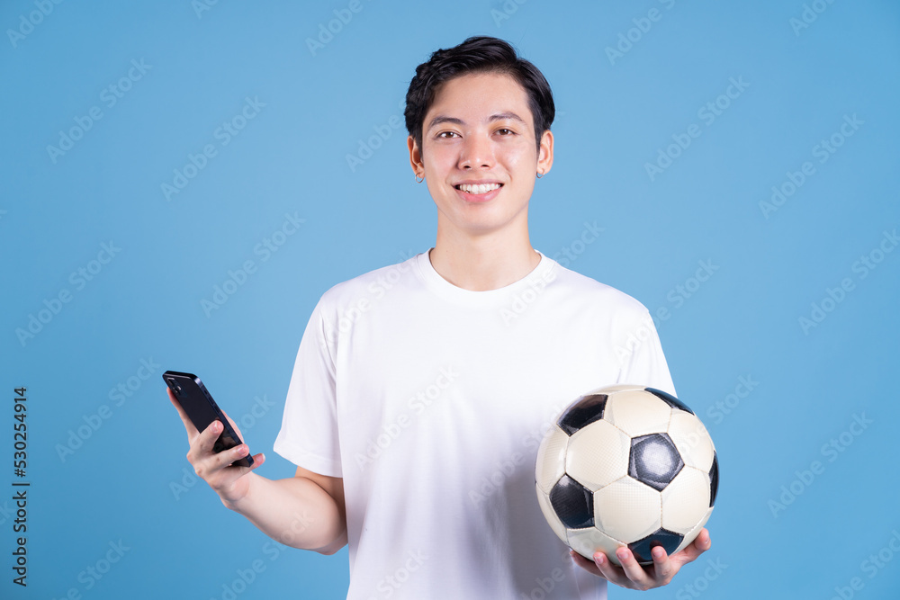 Wall mural Young Asian man holding ball on background