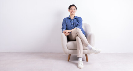 Young Asian man sitting on armchair on white background