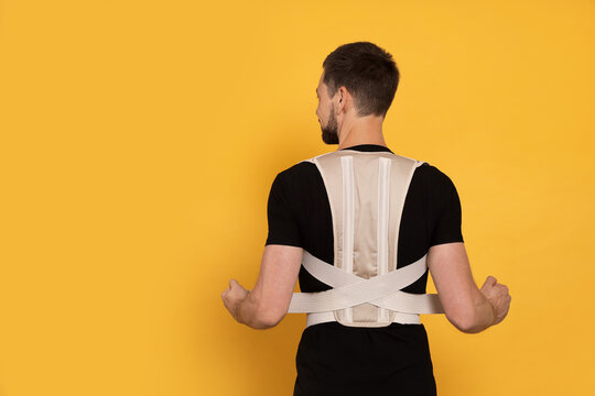 Man with orthopedic corset on orange background, back view. Space for text
