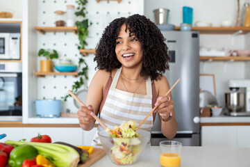 Close up photo of a smiling young woman makes a fresh vegan salad while she uses olive oil for it.