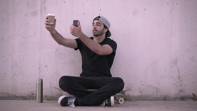 Stylish man takes picture of coffee cup sitting on his skateboard - wide shot