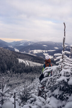 Candid portrait of young smiling man wearing colourful winter hiking jacket, warm-ups and white cap overlooking the snowy area of Stare hamry with the highest point of the Beskydy Mountains Lysa hora