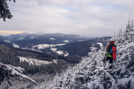 Candid portrait of young smiling man wearing colourful winter hiking jacket, warm-ups and white cap overlooking the snowy area of Stare hamry with the highest point of the Beskydy Mountains Lysa hora