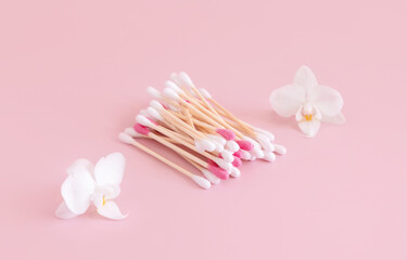 Bamboo cotton buds near white orchid flowers on light pink, Mockup. Skincare product