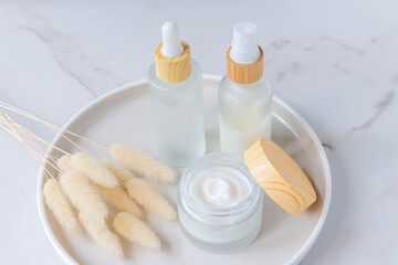 SPA natural organic cosmetics packaging design. Set of transparent glass bottles with bamboo lids, moisturizer cream in wooden jars. with lagurus grass as decoration