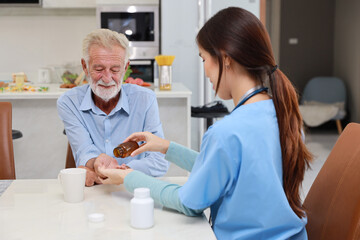Obraz premium Happy caregiver sitting and helping senior caucasian man taking medicine after breakfast in living room at retirement house. Asian smiling nurse taking good help care and support elder patient at home