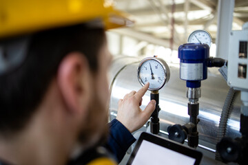 Refinery worker looking at manometer and controlling pressure of natural gas inside pipes.