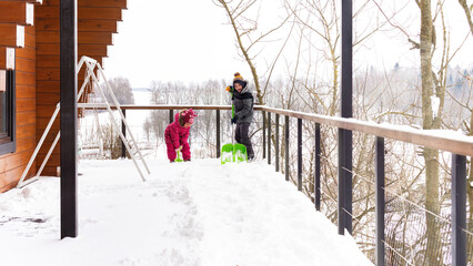 Children clean the terrace of their house with shovels. Little helpers shovel snow. Family...