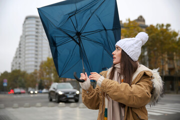 Woman with blue umbrella caught in gust of wind on street