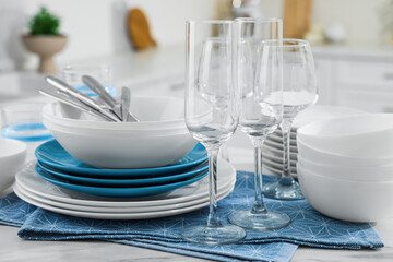 Different clean dishware, cutlery and glasses on white table in kitchen, closeup
