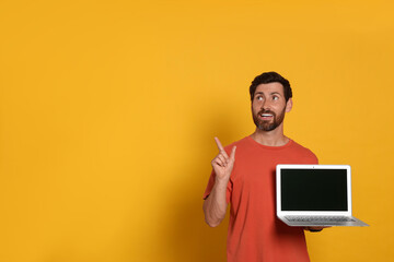 Handsome man with laptop on orange background