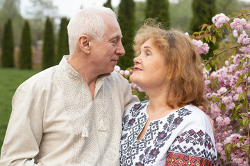 portrait of senior mature couple wearing Ukrainian embroidered shirt standing in park in spring or summer near sakura blooming tree