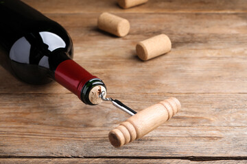 Fototapeta na wymiar Opening wine bottle with corkscrew on wooden table, closeup. Space for text