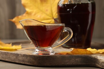 Gravy boat and bottle of tasty maple syrup on wooden table, closeup