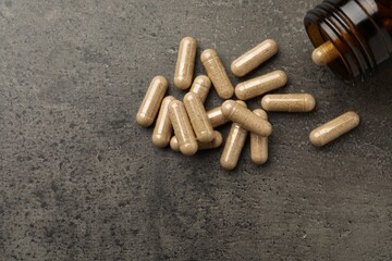 Overturned bottle with dietary supplement capsules on grey table, flat lay. Space for text