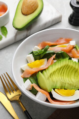 Delicious salad with boiled egg, salmon and avocado served on light grey table, closeup