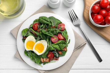 Delicious salad with boiled egg, bacon and tomatoes served on white wooden table, flat lay