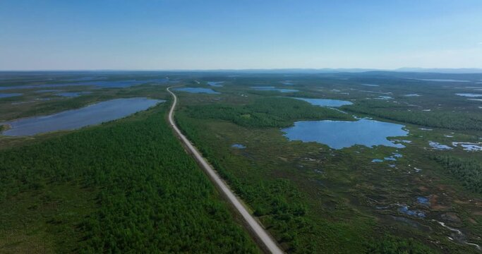 Aerial view of a road in middle of ponds and wetlands of Kevo and Kaldoaivi wilderness, summer in Lapland - tilt, drone shot