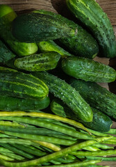 Green farm vegetables cowpea beans and cucumbers on a dark wooden background.