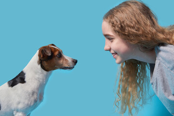 Close-up of a jack russell terrier in profile and a teenage girl looking at each other against a blue background.