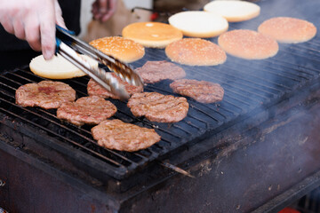 The cook fries meat and heats burger buns on a charcoal grill.
