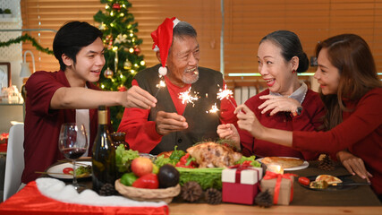 Happy family with sparklers enjoying Christmas eve dinner together in comfortable home. Celebration, holidays and Christmas concept