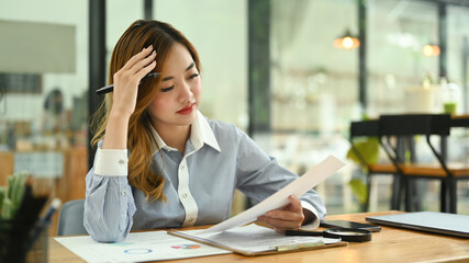 Frustrated female office worker holding her head and reading documents, thinking find solution...