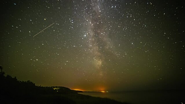 Timelapse shot of star movement along starry night with milky way passing by along seaside.