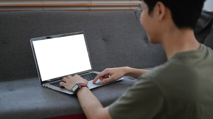 Rear view of asian man sitting in living room and reading email or surfing internet on laptop computer