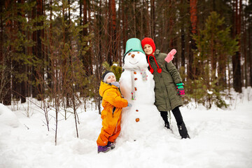 Two sisters make a snowman in winter