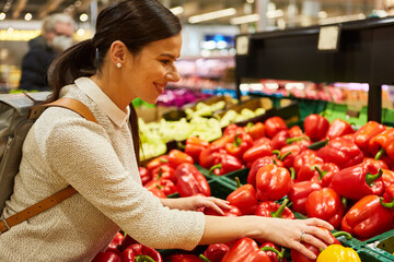 Frau am Gemüsestand im Supermarkt kauft rote Paprika