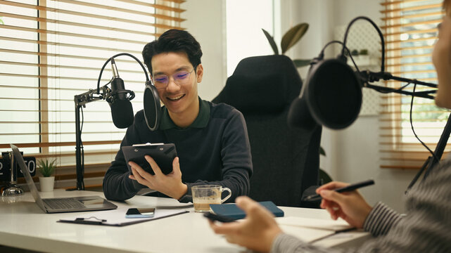Friendly radio host using condenser microphone for recording voice over radio interview guest conversation at home studio