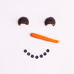 Creative snowman face made with cookies, carrot and buttons on white background. Flat lat Christmas concept
